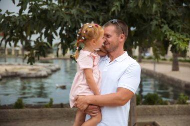 Dad holds his daughter in his arms, a walk in the city park, family leisure