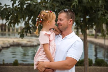 Dad holds his daughter in his arms, a walk in the city park, family leisure