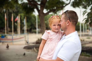 Dad holds his daughter in his arms, a walk in the city park, family leisure