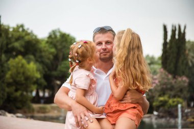 Dad holds two daughters in his arms, a walk in the city park, family leisure