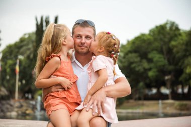 Dad holds two daughters in his arms, a walk in the city park, family leisure
