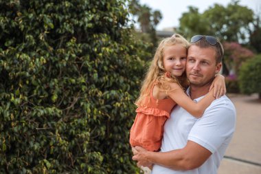 Dad holds his daughter in his arms, a walk in the city park, family leisure