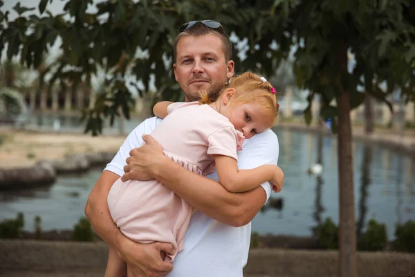 Dad holds his daughter in his arms, a walk in the city park, family leisure