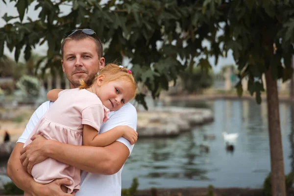 Dad holds his daughter in his arms, a walk in the city park, family leisure