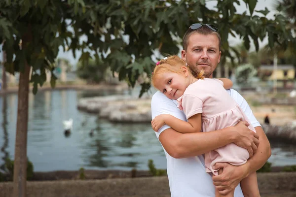 Dad holds his daughter in his arms, a walk in the city park, family leisure
