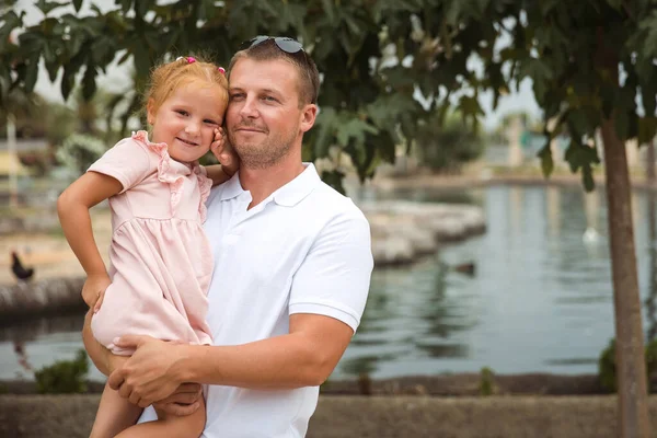 Dad holds his daughter in his arms, a walk in the city park, family leisure