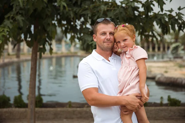 Dad holds his daughter in his arms, a walk in the city park, family leisure