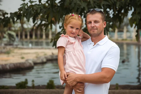 Dad holds his daughter in his arms, a walk in the city park, family leisure