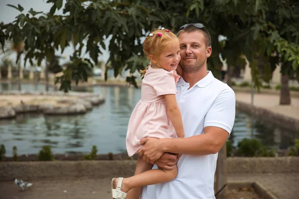 Dad holds his daughter in his arms, a walk in the city park, family leisure