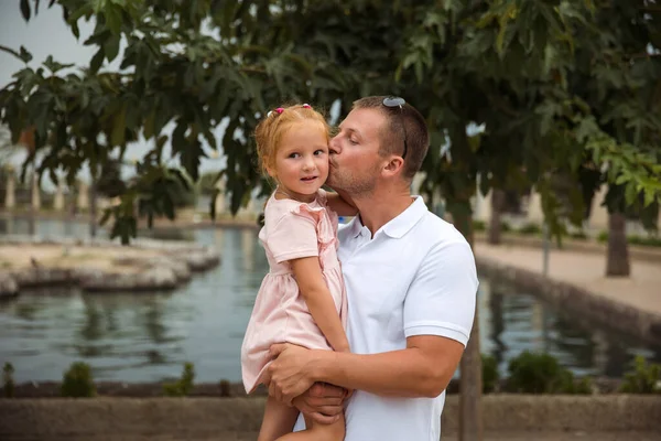 Dad holds his daughter in his arms, a walk in the city park, family leisure