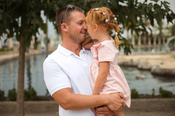 Dad holds his daughter in his arms, a walk in the city park, family leisure
