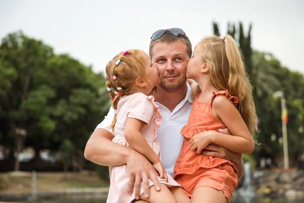 Dad holds two daughters in his arms, a walk in the city park, family leisure