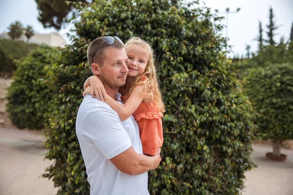 Dad holds his daughter in his arms, a walk in the city park, family leisure