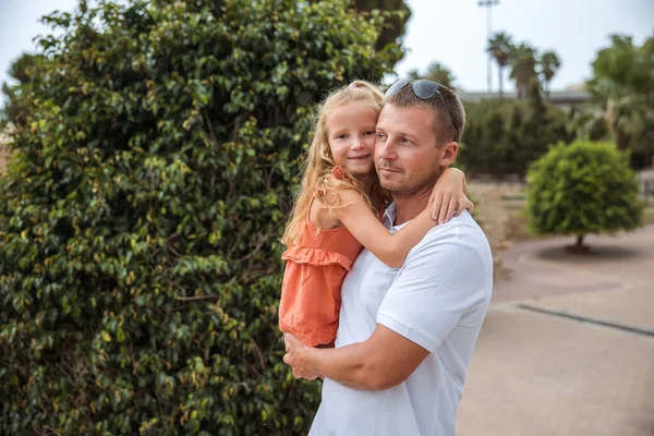 Dad holds his daughter in his arms, a walk in the city park, family leisure