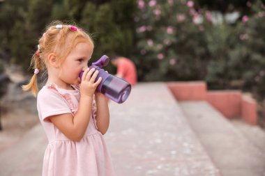 A girl drinks sports bottled water in a city park