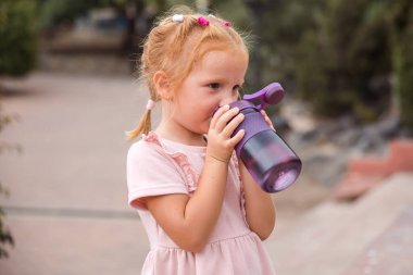 A girl drinks sports bottled water in a city park