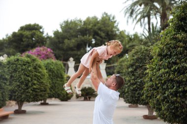 Dad holds his daughter in his arms, a walk in the city park, family leisure