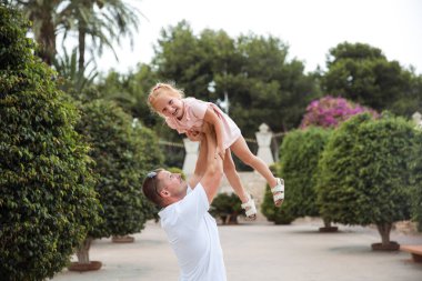 Dad holds his daughter in his arms, a walk in the city park, family leisure