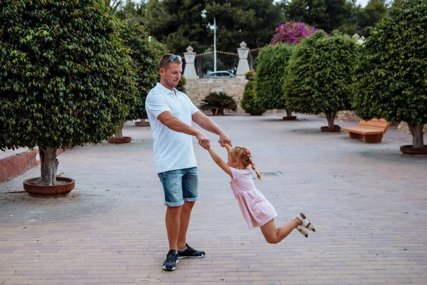 Dad holds his daughter in his arms, a walk in the city park, family leisure
