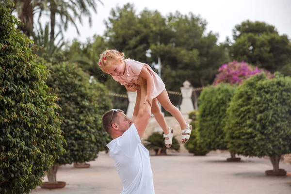 Dad holds his daughter in his arms, a walk in the city park, family leisure