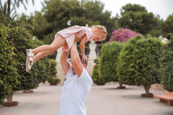 Dad holds his daughter in his arms, a walk in the city park, family leisure