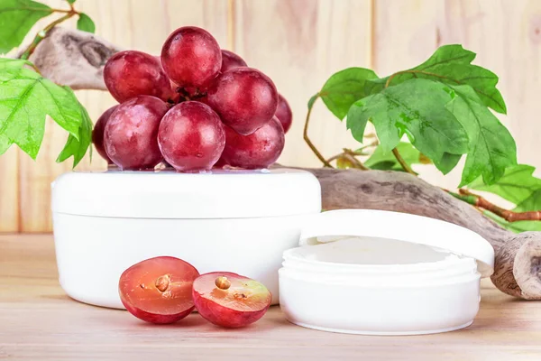 Grape seed cosmetics. Two white jars with a cosmetic product and  red grapes on a wooden background, front view. Organic cosmetic, beauty treatment.