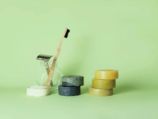 Bamboo toothbrush, steel razor and six natural soaps against green background.