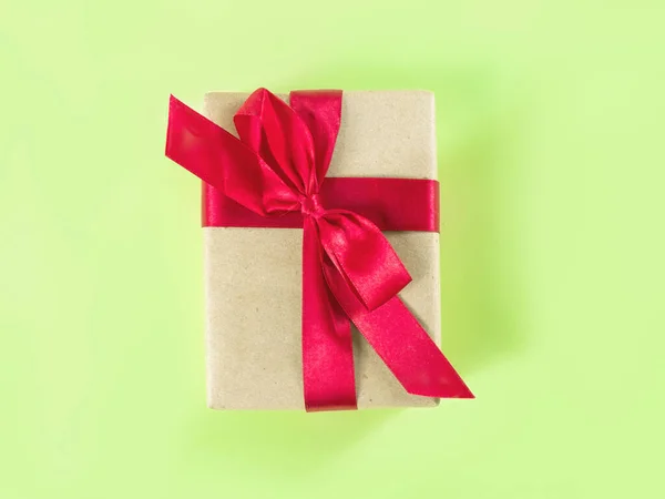 El presente embalado en el papel artesanal con cinta roja sobre el fondo verde. —  Fotos de Stock