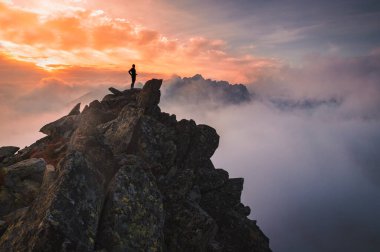 Tepenin zirvesinde tek başına yürüyen bir yürüyüşçü. Arka planda güzel bir sis ve sis var. Gün batımı ışığı