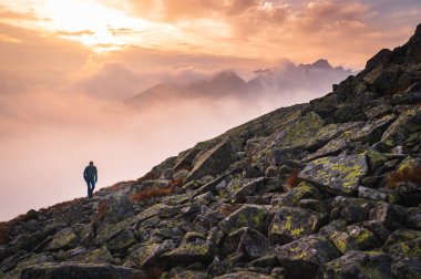 Tepenin zirvesinde tek başına yürüyen bir yürüyüşçü. Arka planda güzel bir sis ve sis var. Gün batımı ışığı