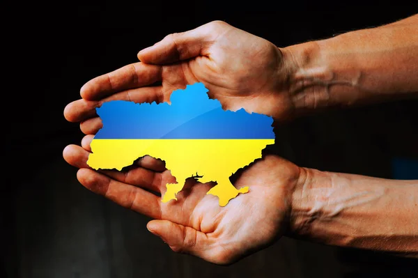 Support for Ukraine in the war with Russia. Hands holding the flag of Ukraine in the shape of the borders of Ukraine.