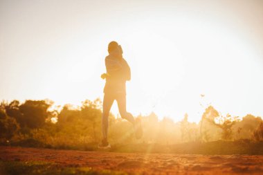 Kenyalı koşucu, gün batımında siluet. Arkaplanda beyaz yüzey