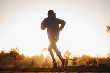 Kenyalı koşucu, gün batımında siluet. Arkaplanda beyaz yüzey