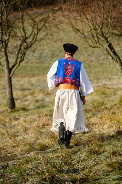 A man dressed in a traditional folk costume. Slovak costume in autumn nature. Old country cottage in the background. Details of Slovak costume from Detva and Hrinova