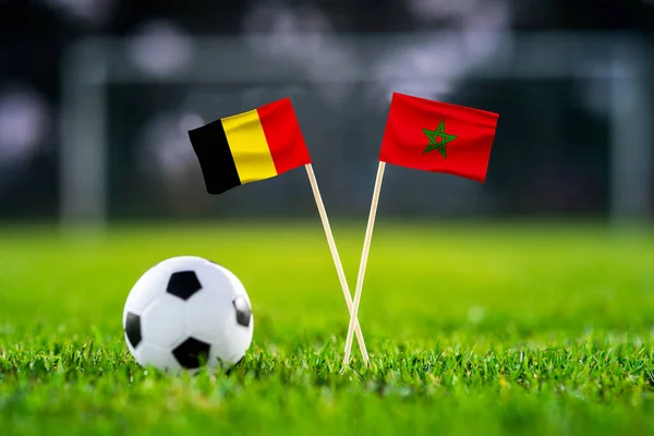 Belgium vs. Morocco, Al Thumama Football match wallpaper, Handmade national flags and soccer ball on green grass. Football stadium in background. Black edit space.