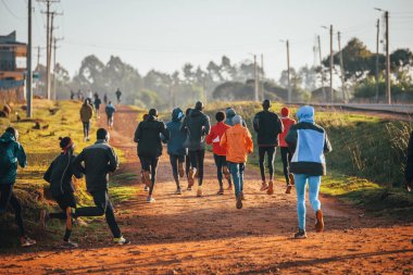 Kenya 'da sabah antrenmanı. Bir grup dayanıklı koşucu gün doğumunda kırmızı toprakta koşuyor. Sabah koşusu motivasyonu.