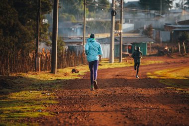 Alone Kenyan woman trains to run in Africa. A female marathon runner runs on red soil in the city of Iten, home of Champions.