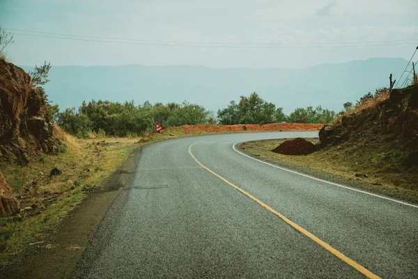 Travel in Africa, grass by the rough road lined with red soil.