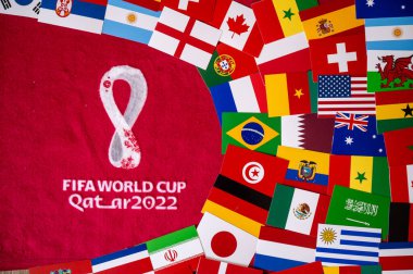 DOHA, QATAR, AUGUST 30, 2022: Flags of all 32 teams participating on FIFA World Cup Qater 2022. Official Logo of Soccer tournament on red background