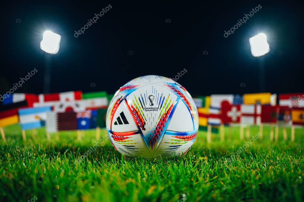 PARIS, FRANCE, 6 SEPTEMBER, 2022: Official Adidas World Cup Football Ball Al Rihla on green grass. Flags of all 32 nations participate on FIFA World Cup in Qatar 2022. Soccer Ball at Stadium in night
