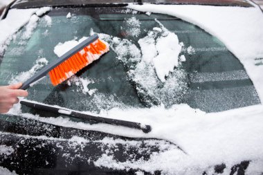 Arabayla ilgili kış sorunları. Bir adam arabayı bir fırçayla kardan temizler.