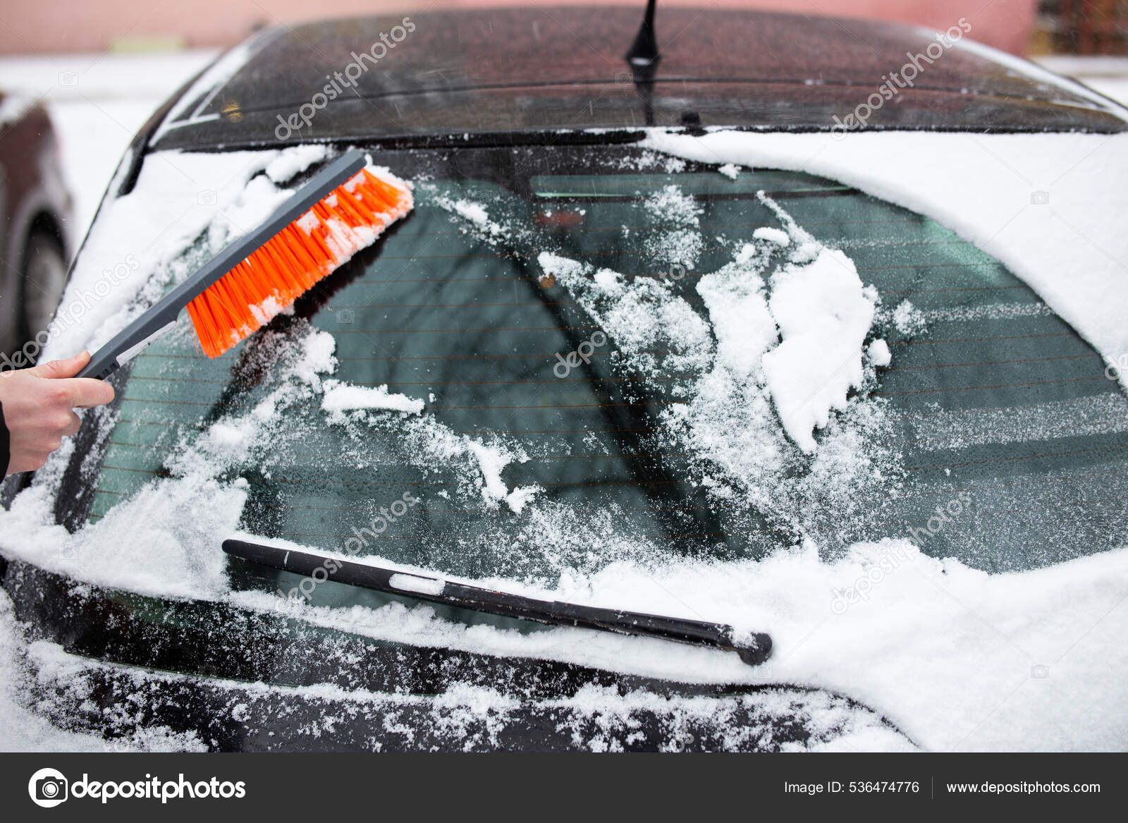 Ein Mann reinigt ein Auto von Schnee mit einem Besen