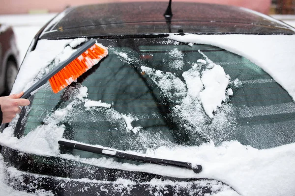 Problemas de inverno com o carro. Um homem limpa o carro da neve com um pincel — Fotografia de Stock