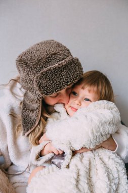Mom and daughter cuddle at home in warm winter clothes