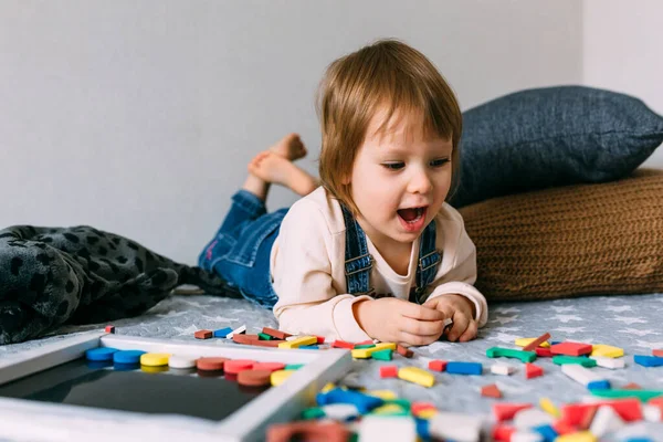 Niño juega en casa un juego educativo con un rompecabezas magnético multicolor —  Fotos de Stock