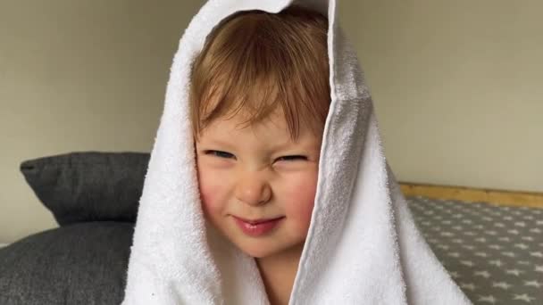 Criança pequena emocionalmente e engraçado poses para câmera em uma toalha branca em sua cabeça — Vídeo de Stock