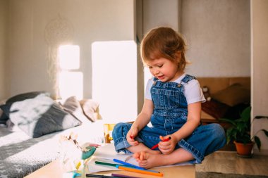 Çocuk masasındaki küçük çocuk keçeli kalemlerle resim çiziyor..