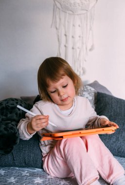 Çocuk teknolojiyi kullanıyor. Evde bir tablet ve kalem stiliyle yürüyen çocuk çiziyor.