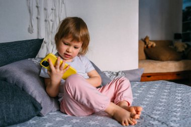 Kanepede oturan küçük bir çocuk akıllı telefon kullanıyor.