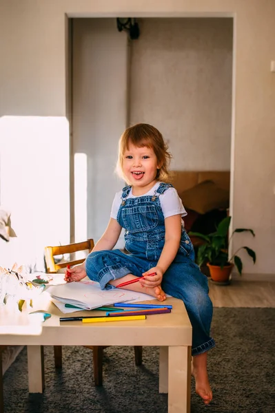 Criança pequena em casa na mesa das crianças desenha com canetas de feltro. — Fotografia de Stock